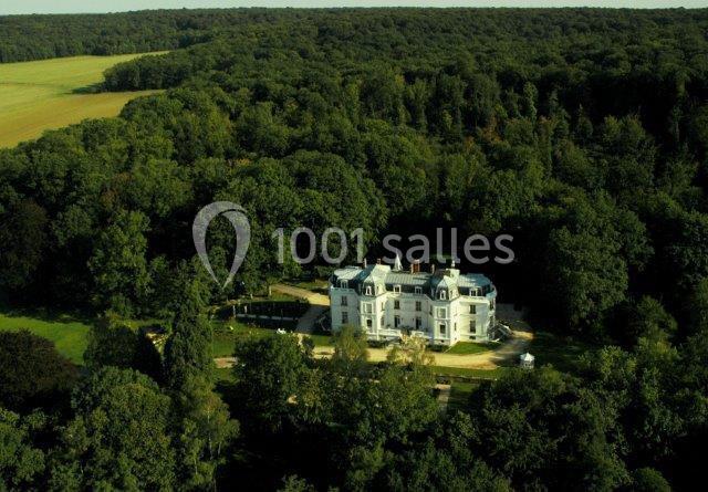 Vue aérienne d'un château blanc entouré de forêt dense et de champs en arrière-plan.