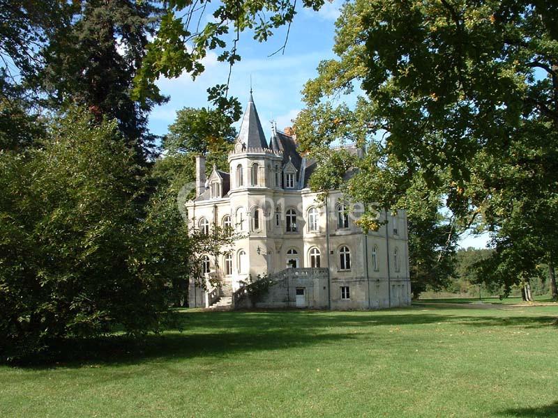 Château entouré d'arbres et d'une pelouse verdoyante sous un ciel bleu.