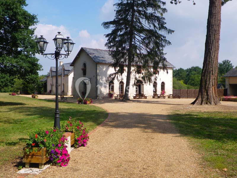 Allée gravillonnée menant à une petite chapelle entourée d'arbres, de fleurs et de bancs en bois.