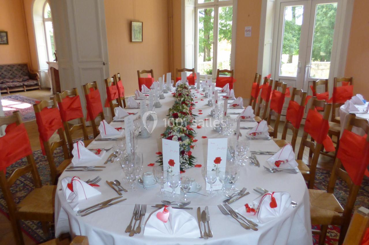 Table dressée pour un repas festif dans une salle lumineuse, avec chaises décorées de nœuds rouges et vaisselle élégante.