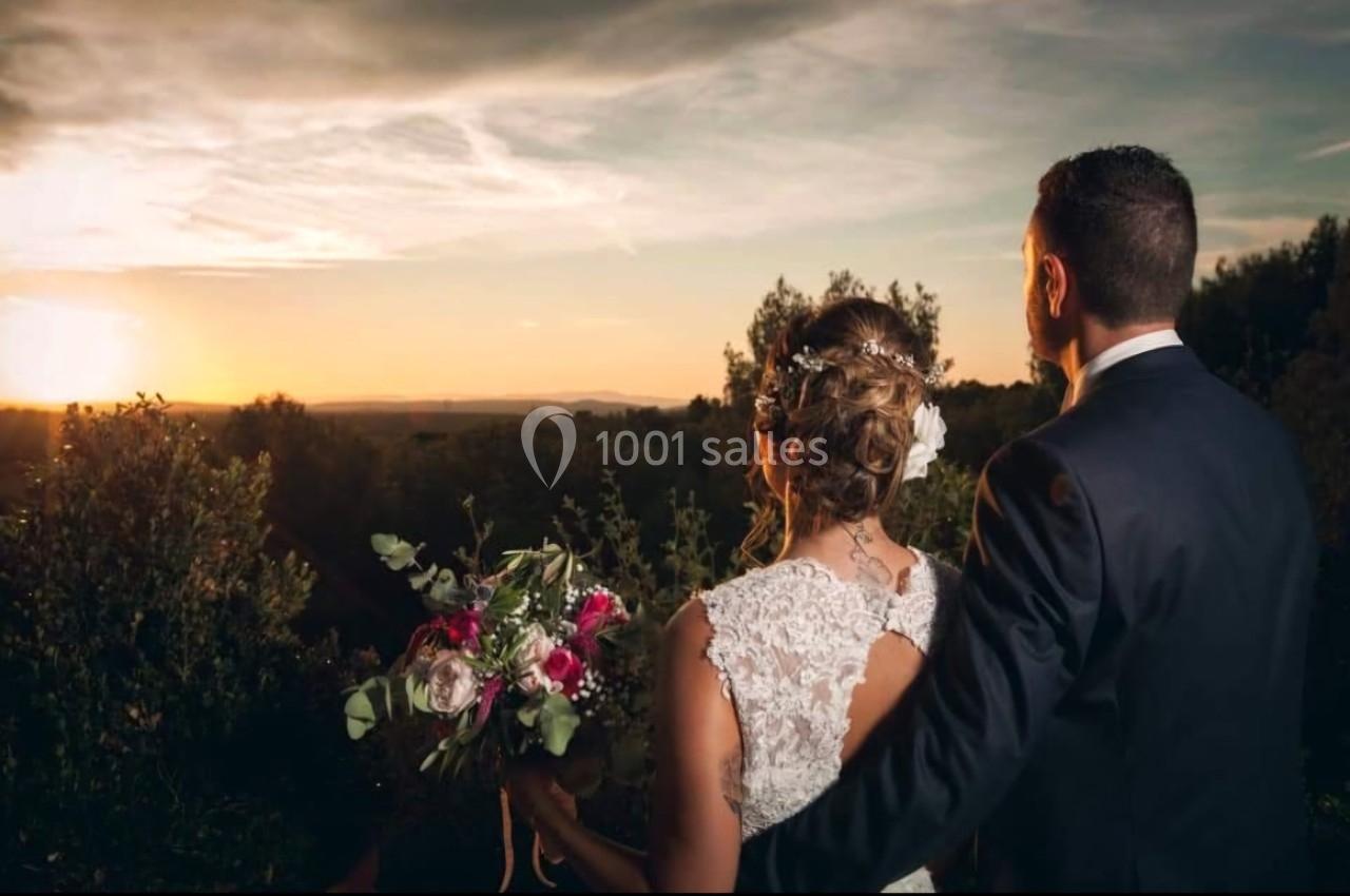 Un couple de dos, vêtu élégamment, regarde un coucher de soleil dans un paysage naturel.