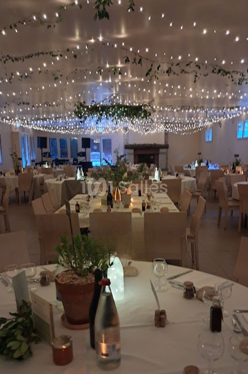 Salle de réception décorée avec des guirlandes lumineuses, des tables dressées et des plantes en centre de table.
