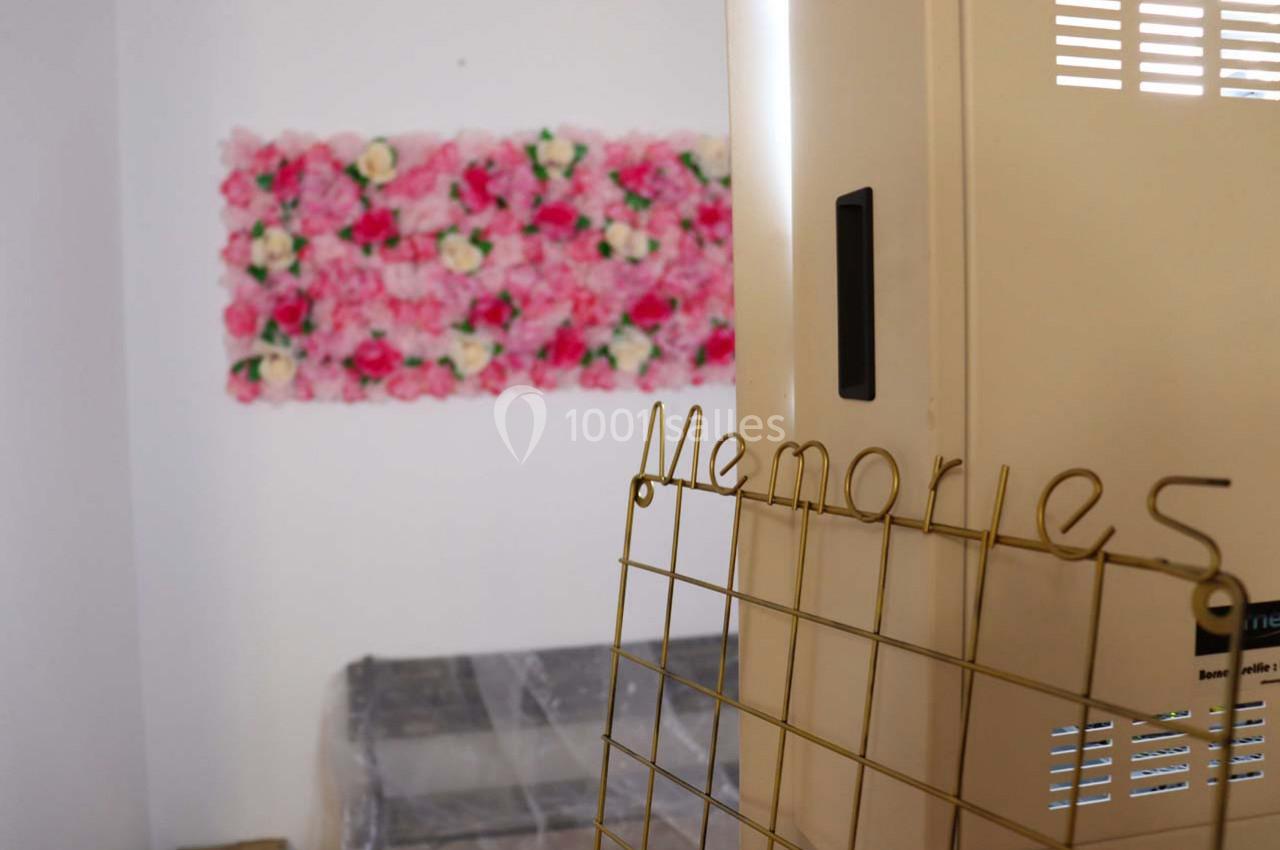 Mur décoré de fleurs roses en arrière-plan, grille métallique dorée avec le mot ’Memories’ au premier plan.