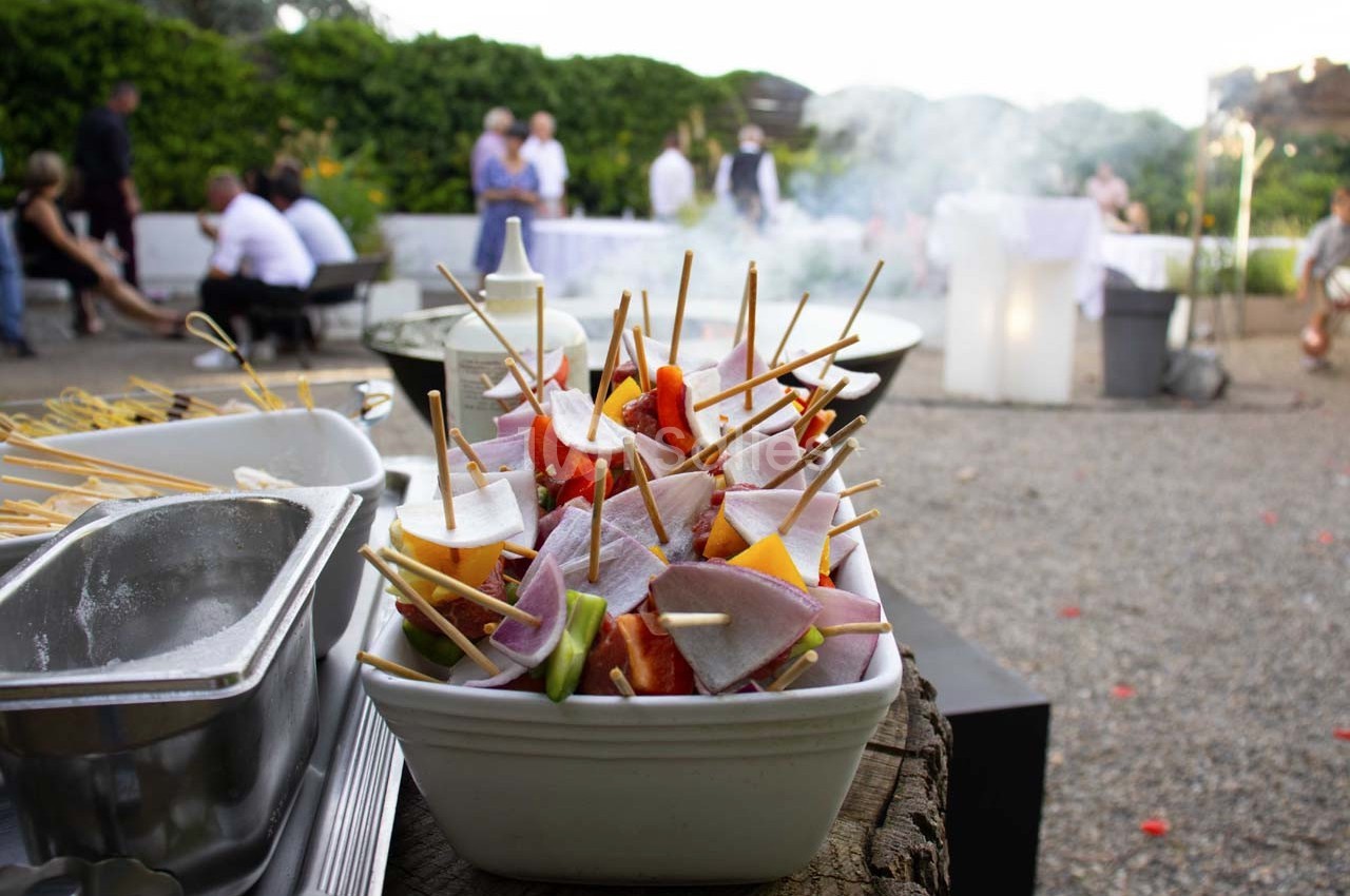 Brochettes de légumes et de charcuterie disposées dans un plat lors d'un événement en extérieur.