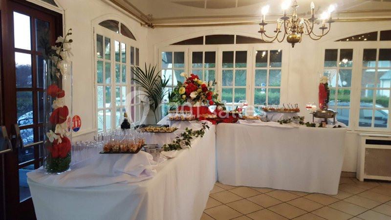 Buffet décoré avec des fleurs, composé de plats variés et disposé dans une salle lumineuse avec des fenêtres vitrées.
