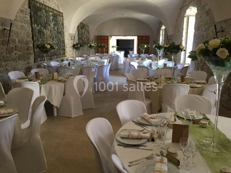 Salle de réception en pierre avec tables rondes et rectangulaires décorées de nappes blanches et compositions florales.