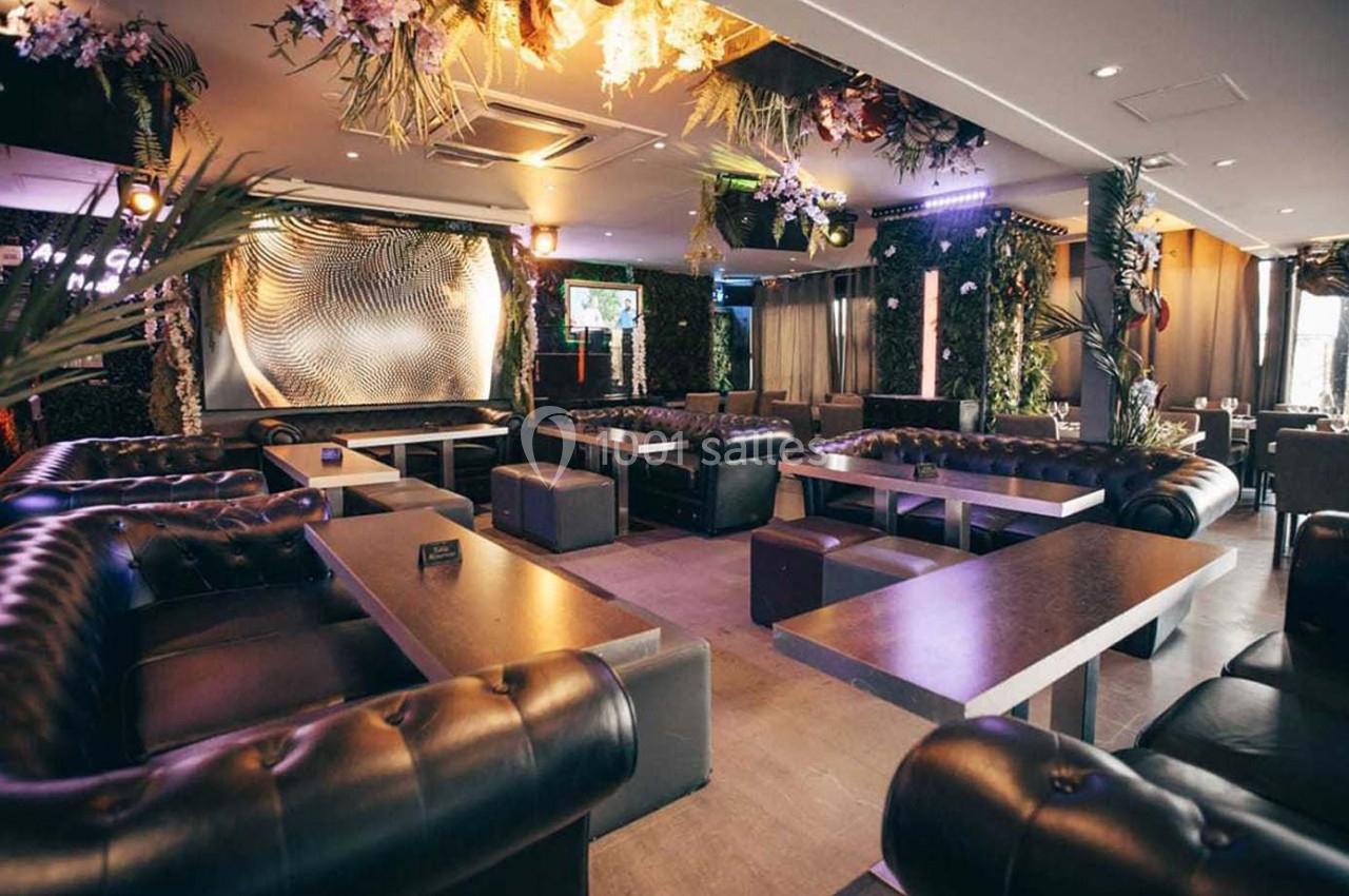 Salon moderne avec canapés en cuir, tables en bois et décoration végétale suspendue dans un éclairage tamisé.