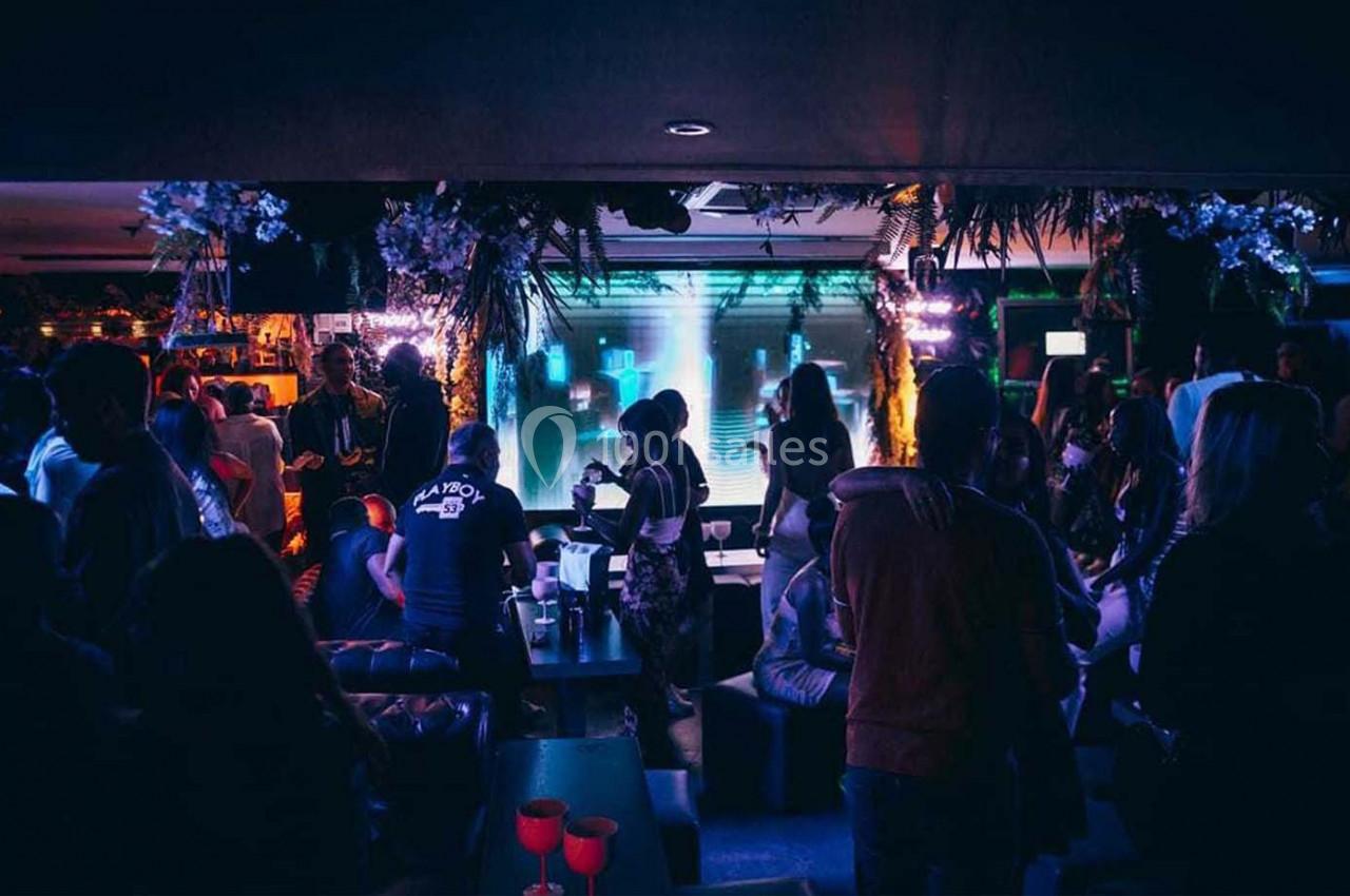 Personnes rassemblées dans un bar ou club, éclairé par des lumières colorées et une ambiance festive.