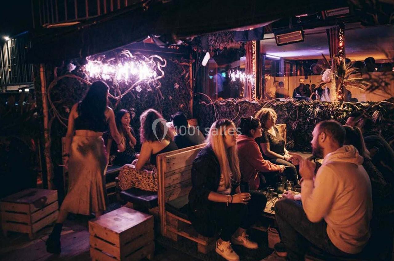 Groupe de personnes discutant et partageant un moment convivial dans un bar à l'ambiance tamisée et chaleureuse.
