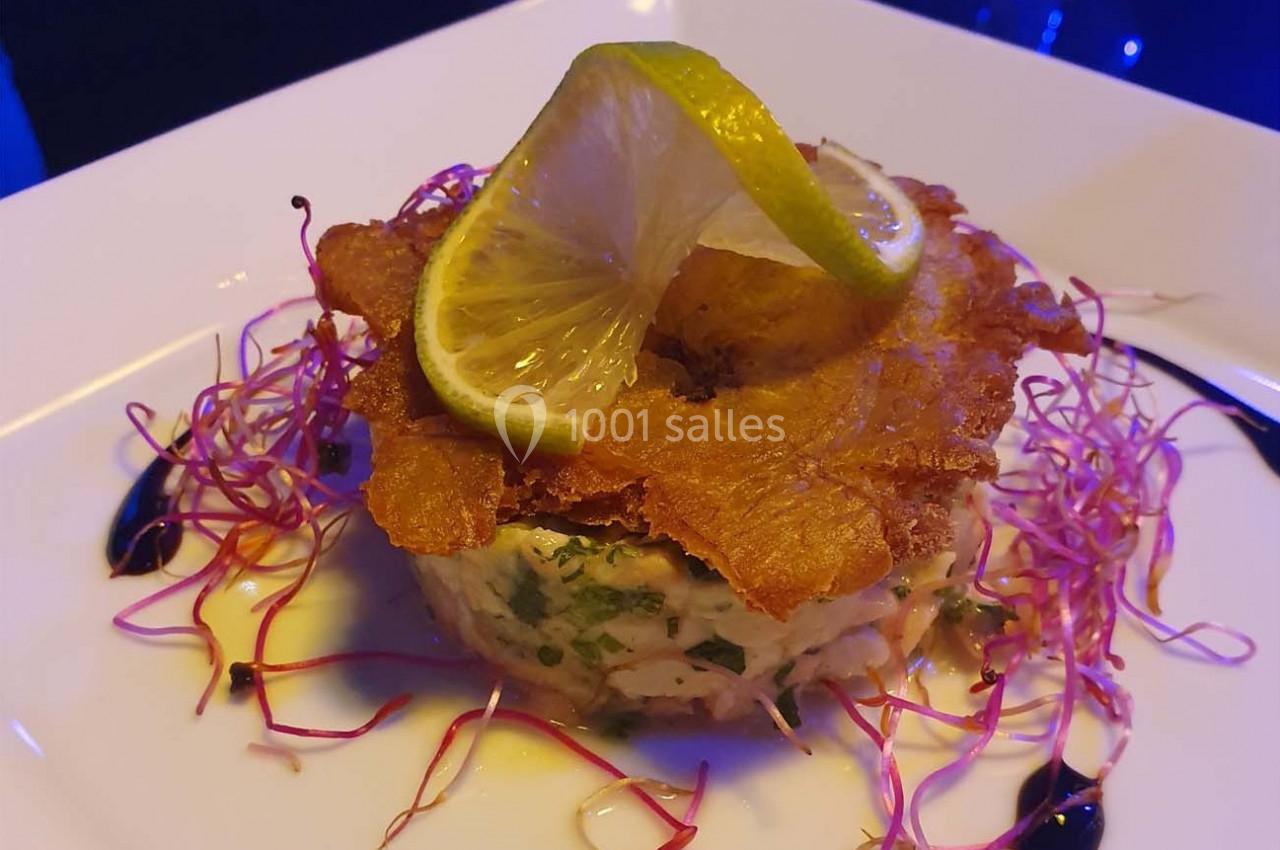 Tartare de poisson garni de chips croustillantes, rondelles de citron et pousses, présenté sur une assiette blanche.