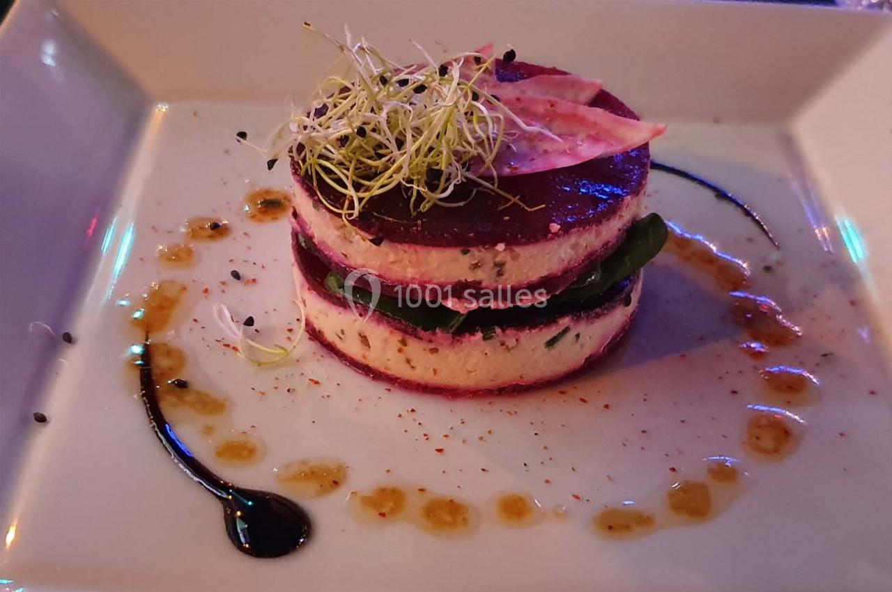 Entrée végétarienne dressée en millefeuille avec betterave, fromage et pousses, entourée de sauces décoratives.