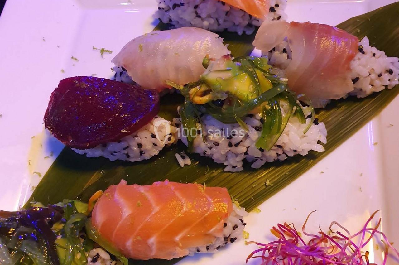 Assortiment de sushis sur une feuille verte, garnis de poisson cru, algues et accompagnés de pousses colorées.