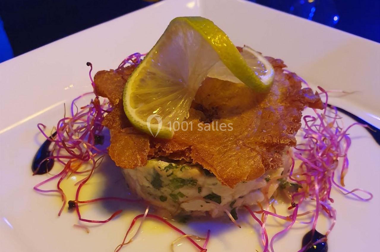 Tartare de poisson garni d'une chips croustillante, tranche de citron et pousses, présenté sur une assiette blanche.