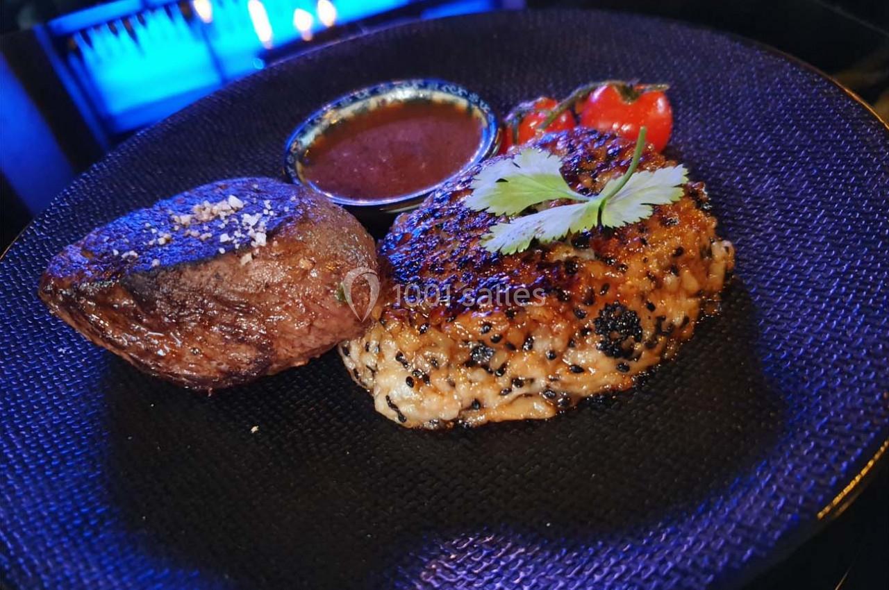 Assiette contenant un steak grillé, une pomme de terre rôtie, une sauce et des tomates cerises en garniture.