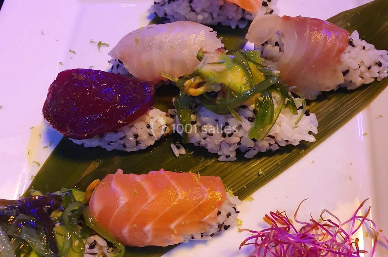 Assortiment de sushis sur une feuille de bambou, garnis de poisson cru, algues et légumes colorés.