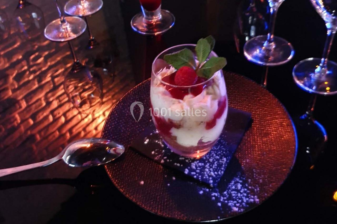 Verrine de dessert avec crème, coulis de fruits rouges, framboise et menthe, servie sur une assiette noire.