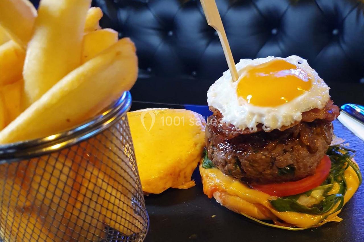 Burger garni d'un œuf au plat, bacon, légumes et fromage, accompagné de frites dans un panier métallique.