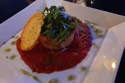 Miniature Location salle Paris 15 (Paris) - Tout Le Monde En Parle Montparnasse #20 Assiette de viande garnie de roquette et sauce rouge, servie sur une table avec des verres de vin en arrière-plan.