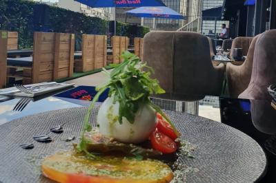Miniature Location salle Paris 15 (Paris) - Tout Le Monde En Parle Montparnasse #21 Assiette de viande garnie de roquette et sauce rouge, servie sur une table avec des verres de vin en arrière-plan.