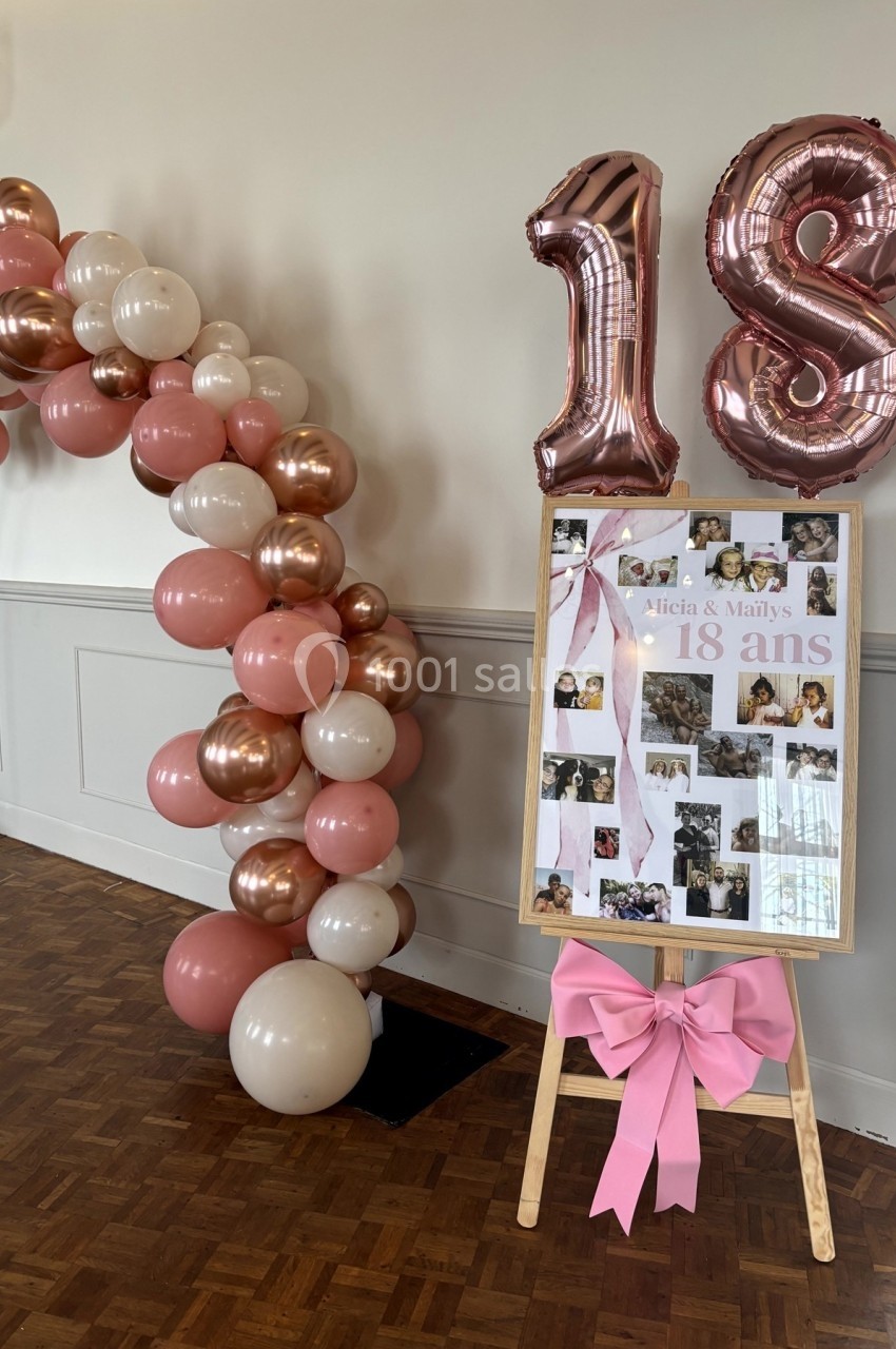 Décoration d'anniversaire avec arche de ballons roses et dorés, panneau photo sur chevalet et ballons ’18’.