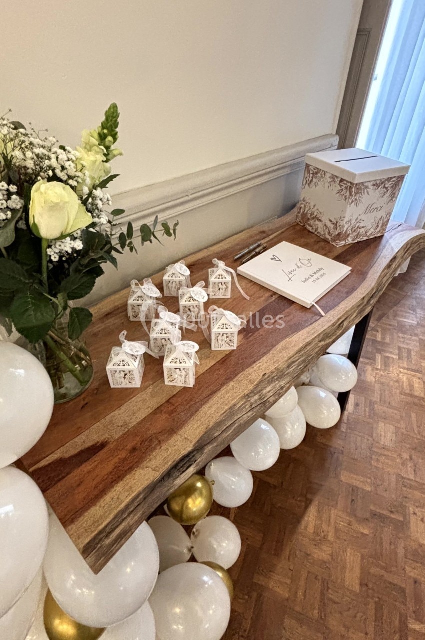 Table décorée avec des ballons blancs et dorés, un bouquet de fleurs, des boîtes cadeaux et une urne pour cartes.