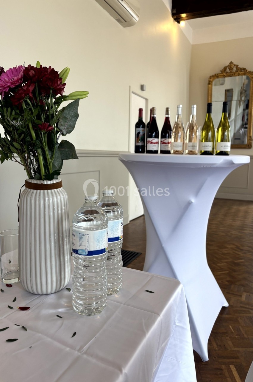 Vase de fleurs, bouteilles d'eau et assortiment de vins sur des tables dans une salle lumineuse avec miroir mural.