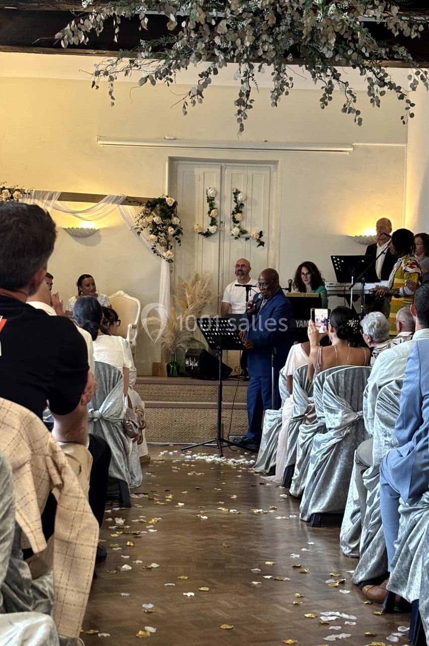Cérémonie dans une salle décorée, avec un homme parlant au micro devant des invités assis et un groupe musical.