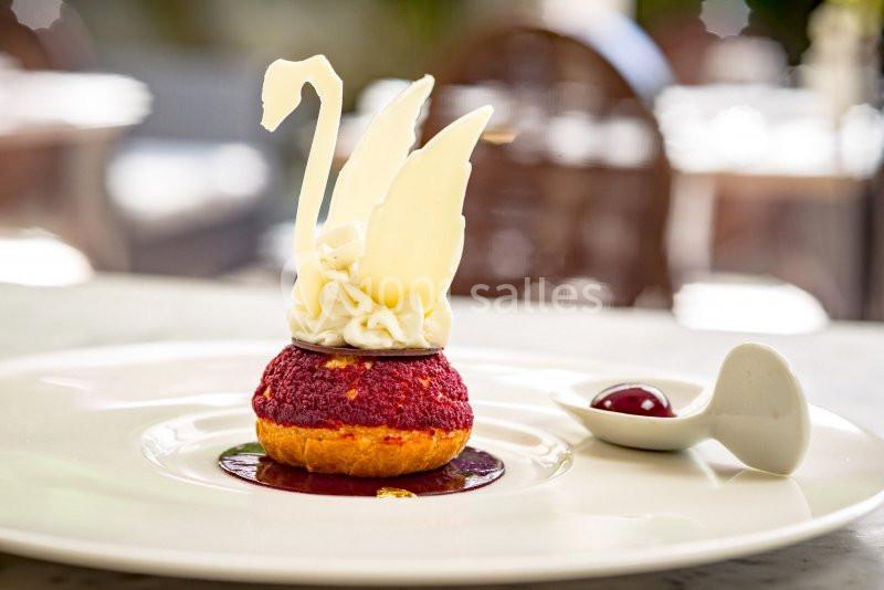 Pâtisserie en forme de cygne avec ailes en chocolat blanc, posée sur une assiette avec une cuillère contenant une cerise.