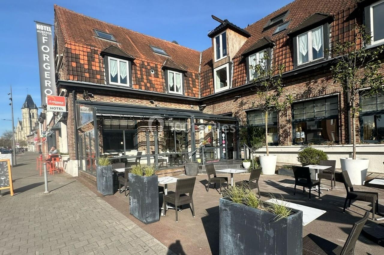 Terrasse extérieure d'un restaurant avec tables et chaises, devant un bâtiment en briques avec toit en tuiles.