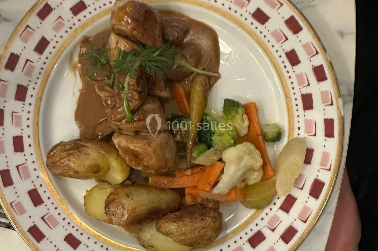 Assiette garnie de viande en sauce, pommes de terre rôties et légumes variés sur une table en marbre.