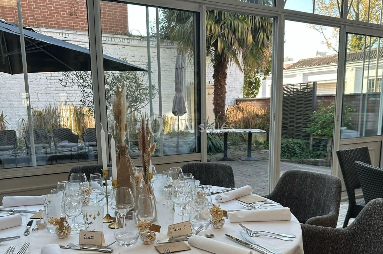 Table élégamment dressée avec vaisselle et décorations, située dans une salle lumineuse donnant sur un jardin.