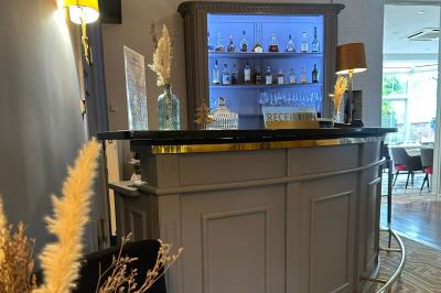 Comptoir de réception en bois avec étagères éclairées contenant des bouteilles et des verres, décoré de plantes séchées.