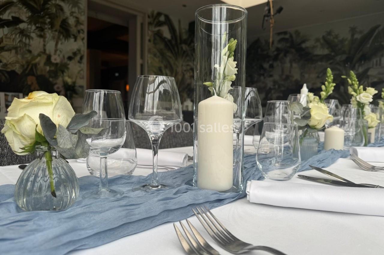 Table élégamment dressée avec nappe blanche, verres, couverts, bougies et décorations florales dans un cadre raffiné.