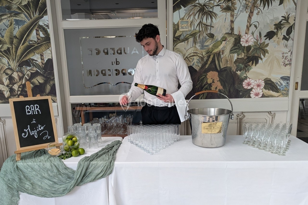 Serveur versant une boisson dans un verre sur une table dressée avec des verres, des citrons et un seau à glace.