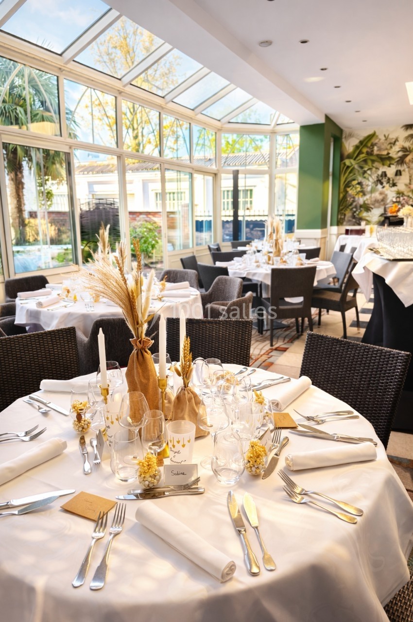 Salle de réception lumineuse avec tables élégamment dressées, décorées de bougies et d'éléments naturels.