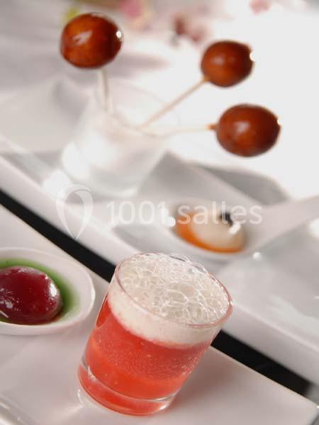 Verre de mousse rose accompagné de sucettes et de petites sauces colorées sur un plateau blanc.