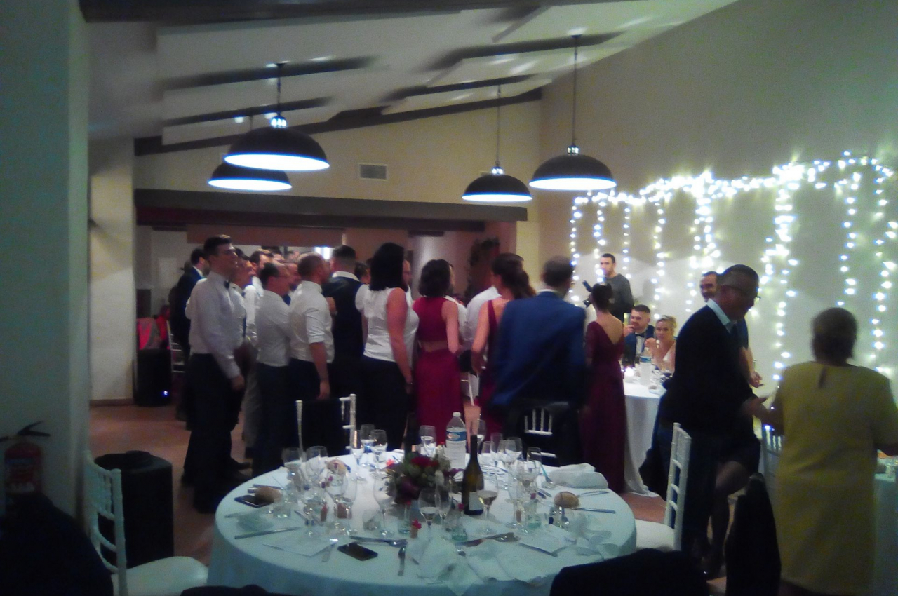 Groupe de personnes debout et discutant dans une salle de réception décorée avec des guirlandes lumineuses.