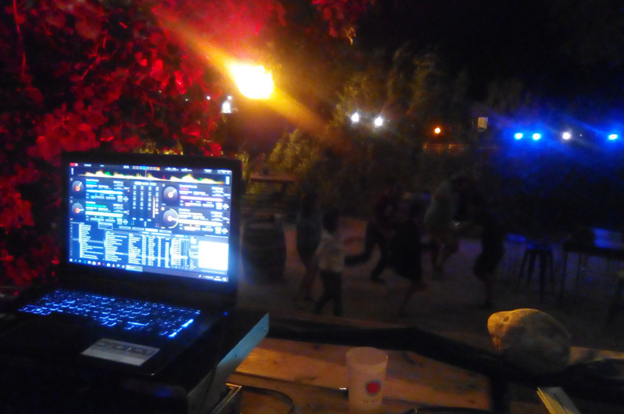 Ordinateur portable affichant un logiciel de DJ, avec des personnes dansant en arrière-plan dans un espace extérieur…