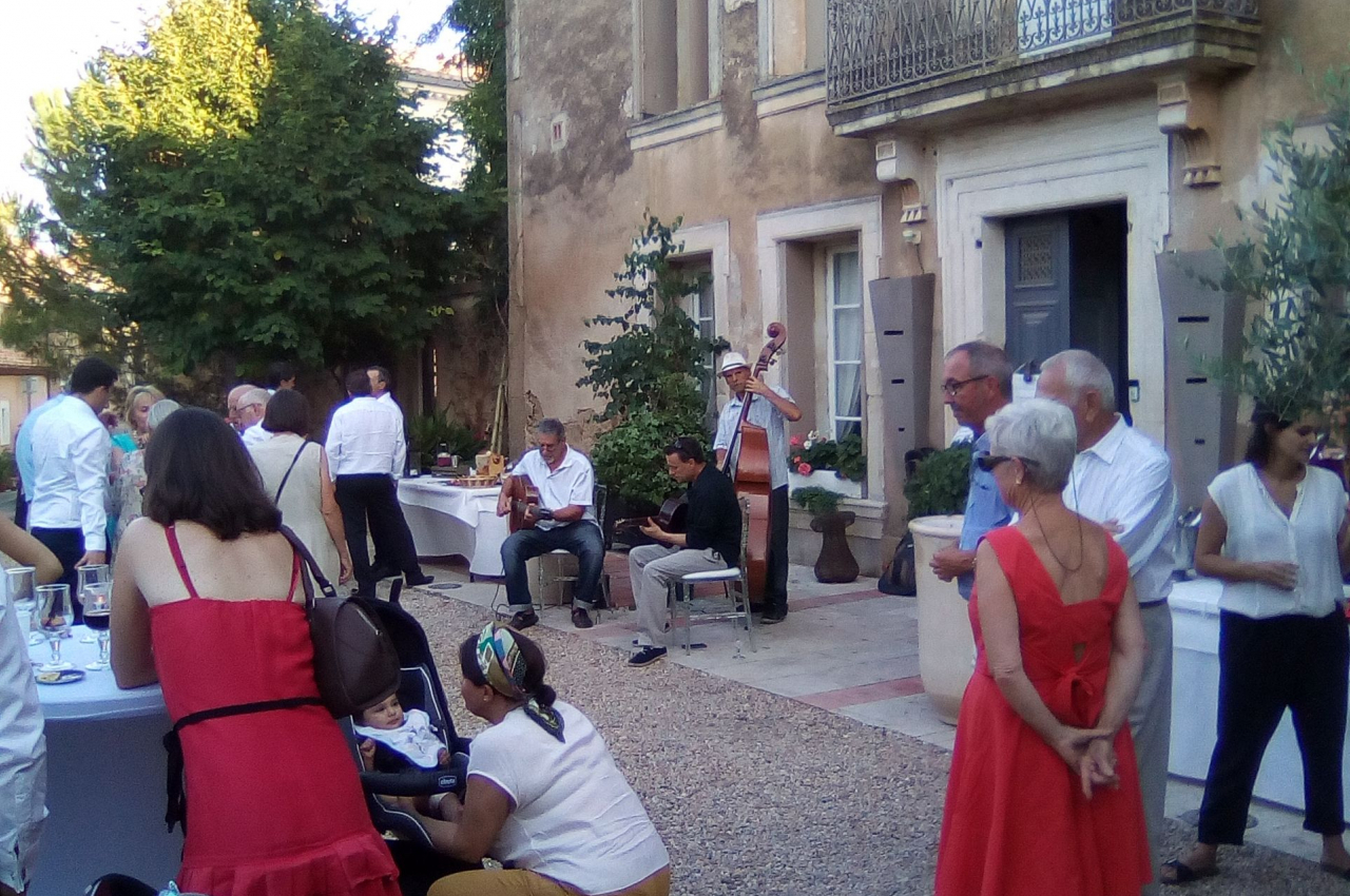 Des personnes rassemblées dans une cour extérieure devant un bâtiment ancien, certaines discutant près de tables.