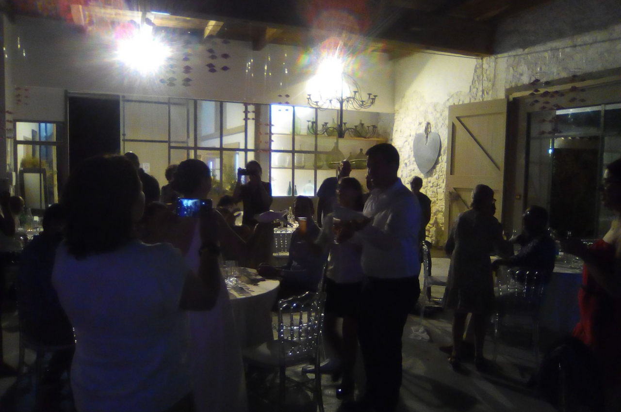 Des personnes rassemblées dans une salle faiblement éclairée, discutant et prenant des photos lors d'un événement.