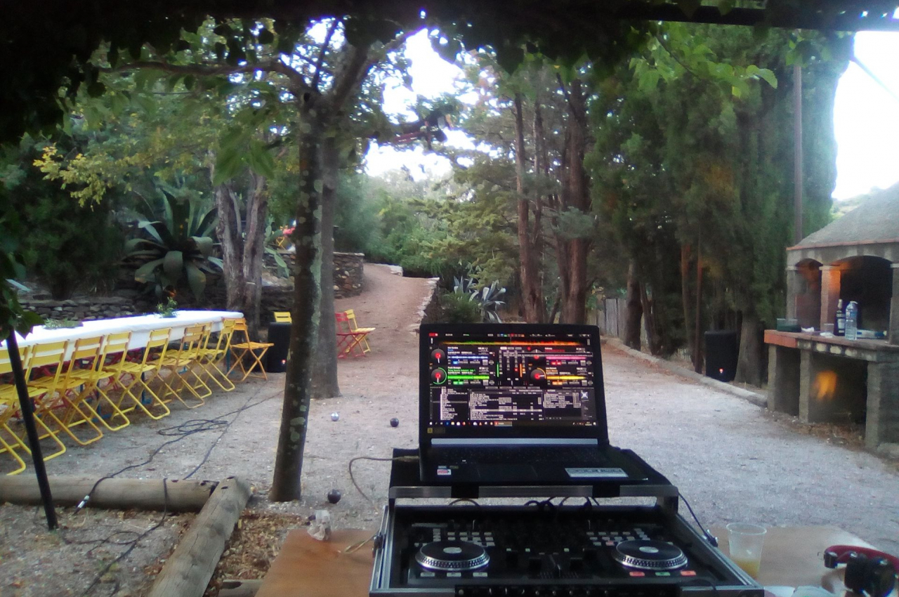 Ordinateur portable avec logiciel de mixage installé, posé sur une table en extérieur près d'une allée bordée d'arbres.