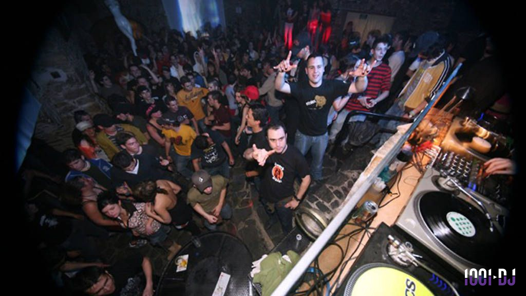 Un DJ anime une soirée dansante avec une foule dense dans une ambiance festive et éclairage tamisé.