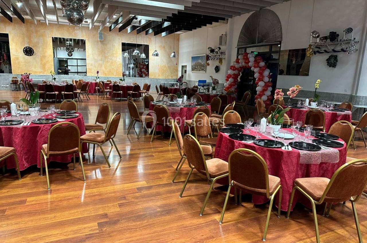 Salle de réception avec tables rondes dressées, nappes rouges, chaises marron et décoration festive en arrière-plan.