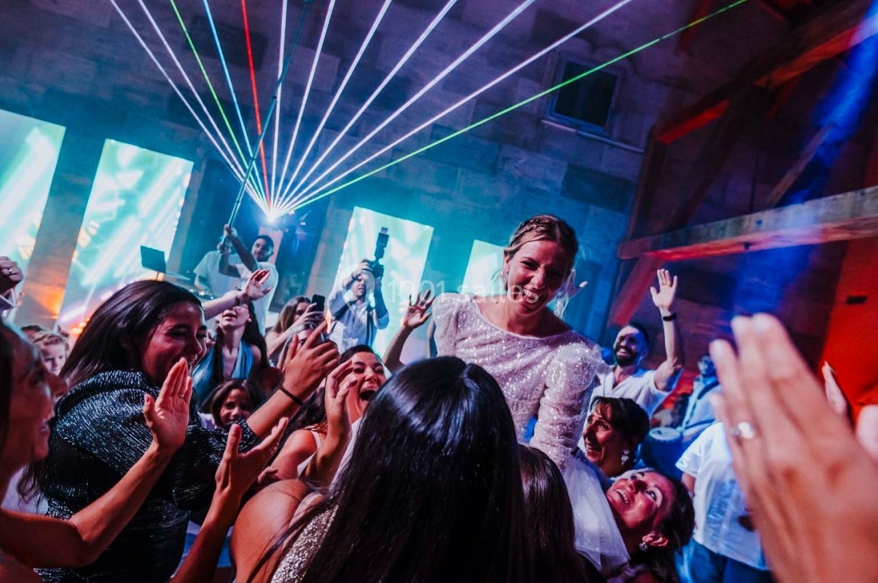 Une mariée souriante entourée d'invités dansant sous des lumières colorées et des faisceaux laser.