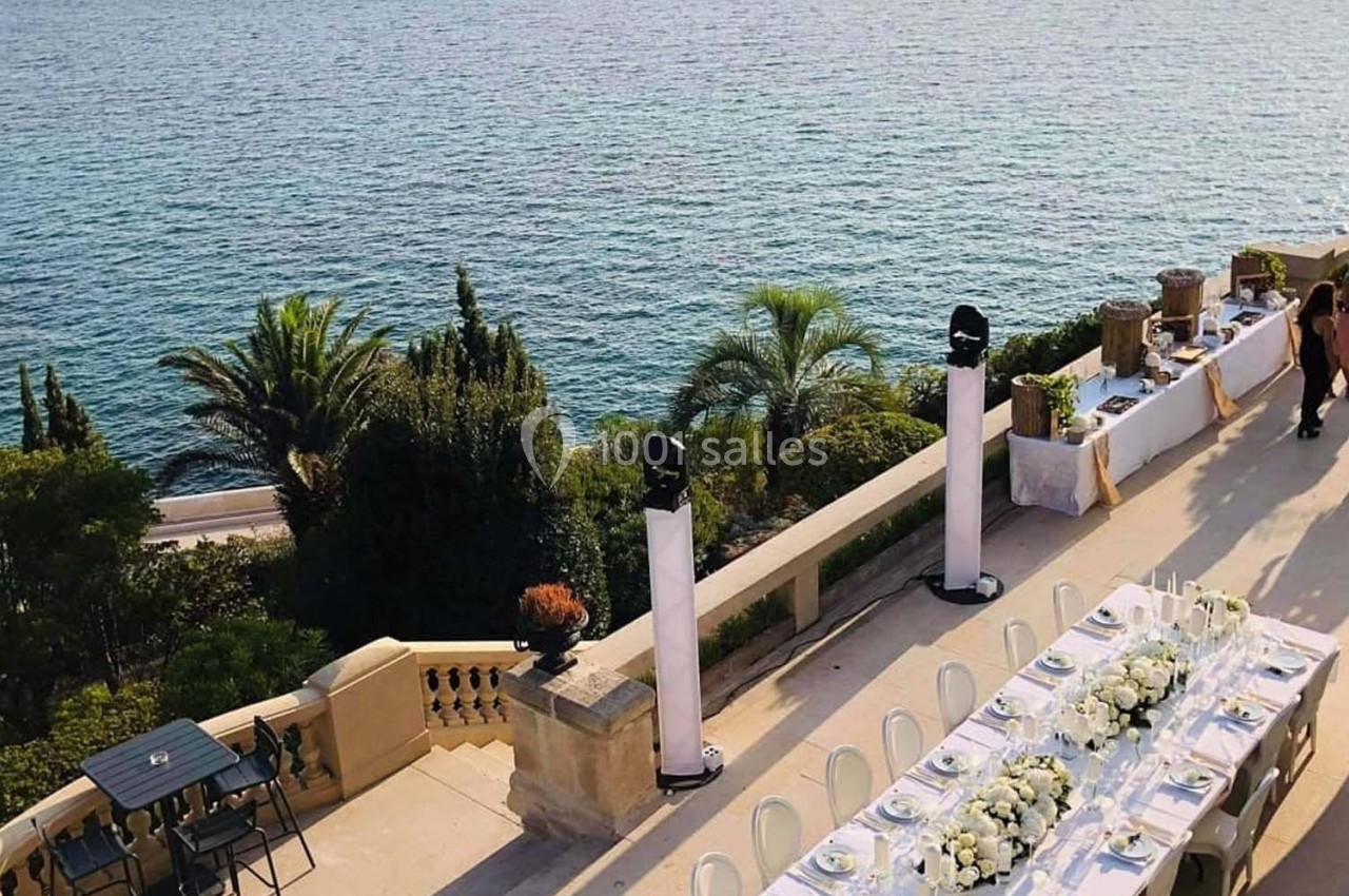 Table décorée pour un événement en extérieur, avec vue sur la mer, des palmiers et une terrasse élégante.
