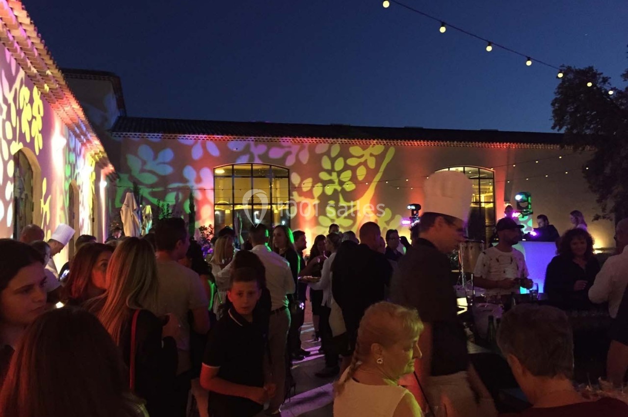Groupe de personnes rassemblées en soirée extérieure, éclairée par des projections colorées sur les murs.