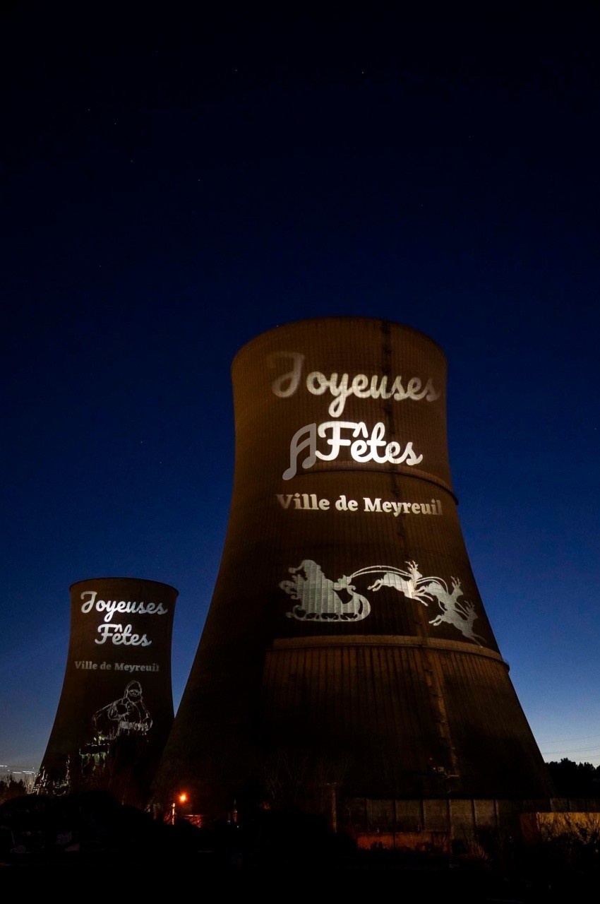 Tours de refroidissement illuminées par des projections de vœux festifs et de motifs décoratifs, de nuit.