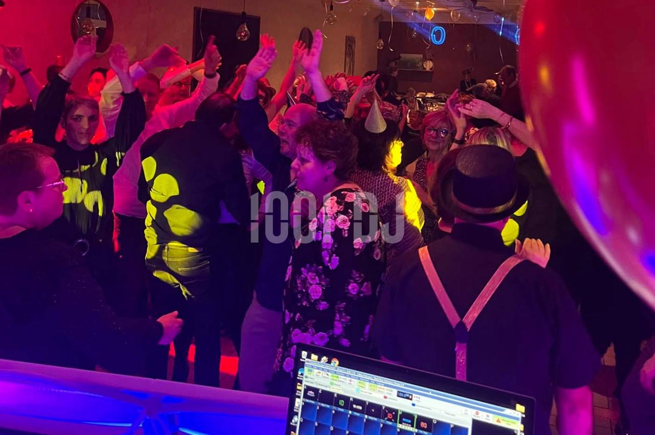 Groupe de personnes dansant sous des lumières colorées lors d'une soirée festive en intérieur.