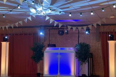 Stand de DJ avec éclairage LED rouge et vert, installé dans une salle avec décoration intérieure et lumière naturelle.