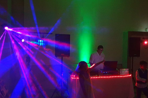 Un DJ anime une soirée avec des jeux de lumière colorés et des participants dansant devant la scène.